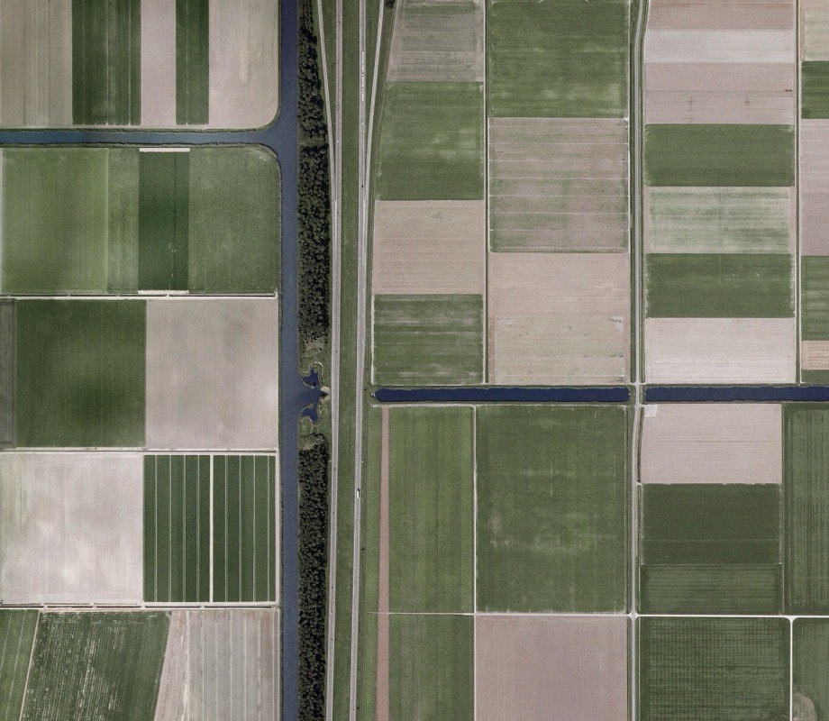 Aerial view of cultivated fields and waterways forming a patchwork grid &mdash; the systems-level view MJ Axiom brings to community work